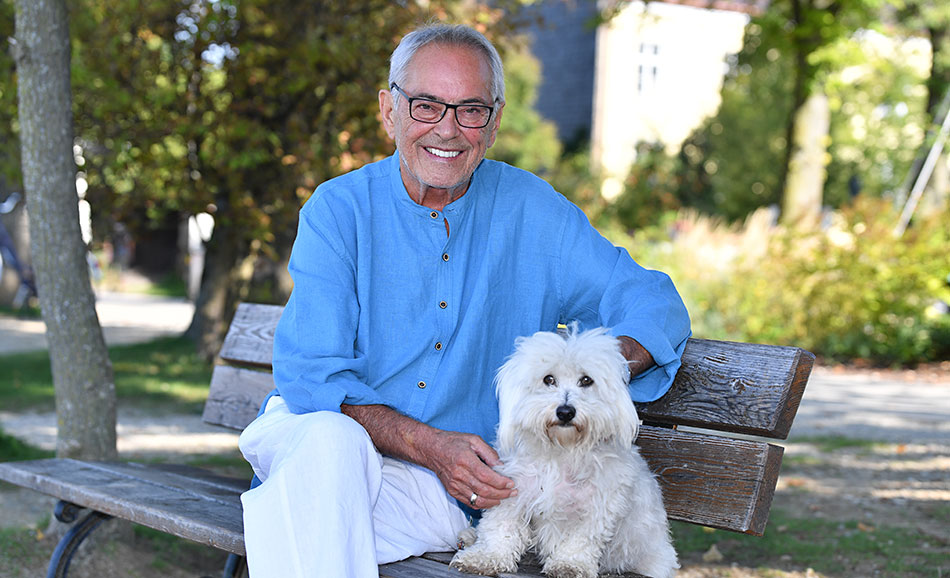 Der Künstler Franco Thamer mit seinem Hund Lui auf einer Parkbank am Chiemsee